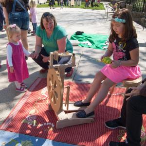 Child using spinning wheel while a family watches